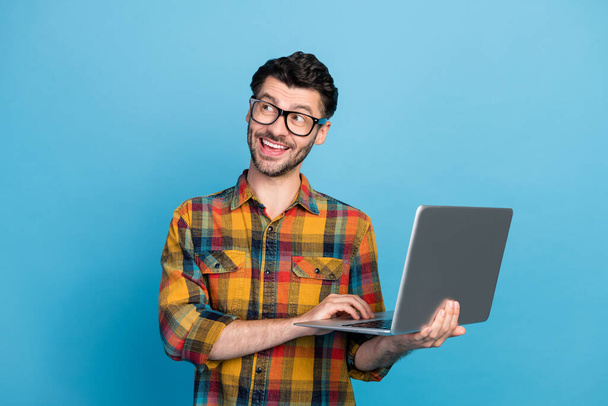 Photo of funny brunet guy hold laptop wear eyewear checkered shirt isolated on blue color background. - Foto, afbeelding