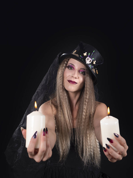 Портрет женщины, смотрящей в камеру на Хэллоуин со свечами в каждой руке, улыбающейся - Фото, изображение