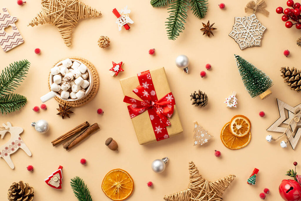 クリスマスの装飾品のトップビューの写真ギフトボックスの泡ウィッカースター木製の装飾ジングルベルアコーン松の枝ココアミステリーのコーンマグカップと孤立したベージュの背景に乾燥柑橘類のスライス - 写真・画像
