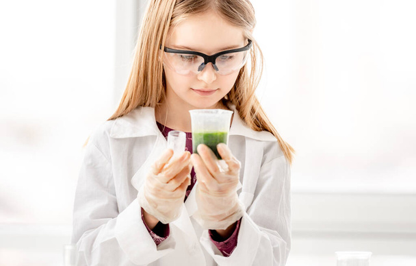 A lány, aki tudományos kémia kísérleteket végez védőszemüveget visel. Iskoláslány felszereléssel és vegyi folyadékkal az iskolai leckén - Fotó, kép