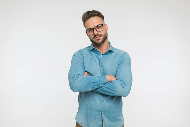 sexy ležérní muž s tvrdým postojem přes ruce a nosí brýle na šedém pozadí - Fotografie, Obrázek