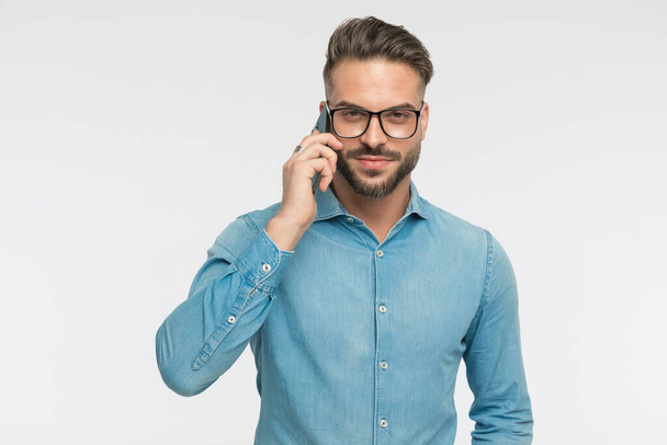 cool casual man talking on the phone, looking at the camera and wearing eyeglasses on gray background - Foto, Bild