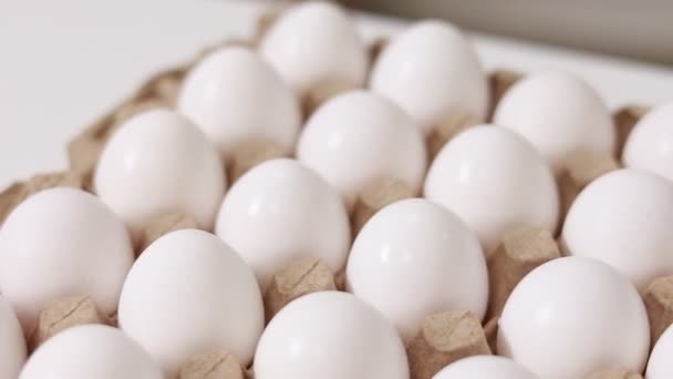 White chicken eggs in a cardboard box. Fresh raw eggs in a paper egg container for store and shop. egg tray with eggs on white table background. Top view. preparation to easter holiday. - Materiał filmowy, wideo