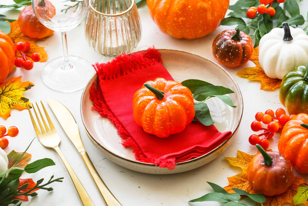 Autumn table setting. Craft plate, golden cutlery, glass, candle and fall decorations. - Photo, Image