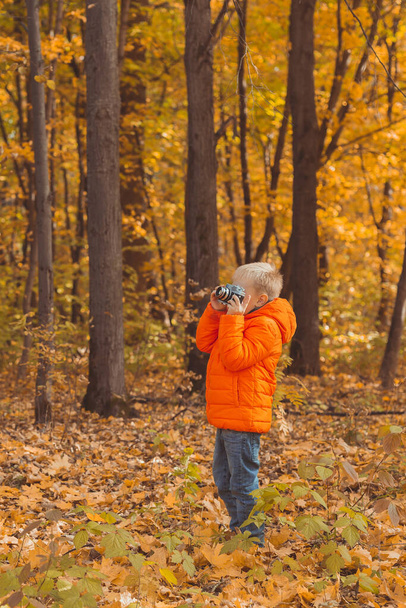 Retro kameralı çocuk sonbahar doğasında dışarıda fotoğraf çekiyor. Boş zaman ve fotoğrafçı konsepti. - Fotoğraf, Görsel