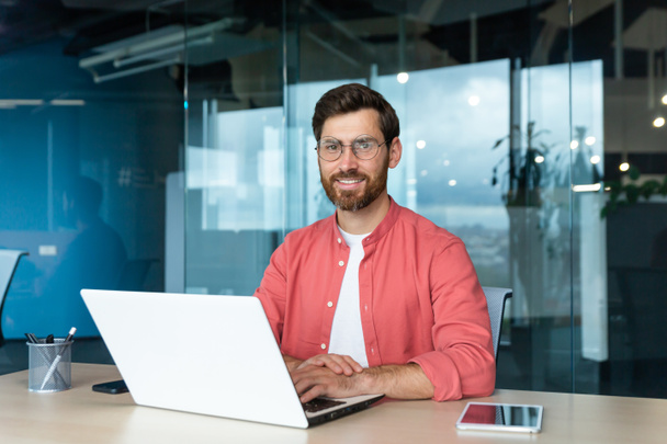 Portrait of mature businessman freelancer startup, bearded man smiling and looking at camera, business owner working inside modern office building wearing red shirt and glasses. - Foto, afbeelding