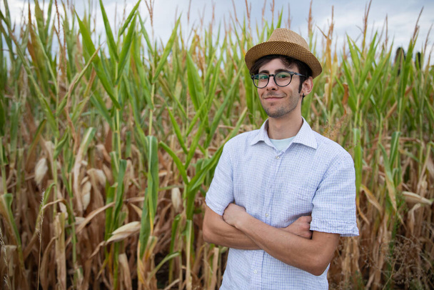 Contadino sorridente con le mani incrociate davanti al suo campo di grano, presto il mais sarà pronto per il raccolto. - Foto, immagini