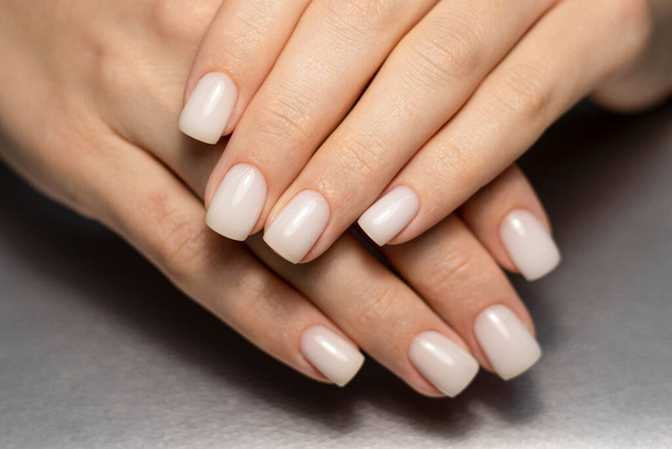 Beautiful nude manicure. Short square nails. Nail design. Manicure with gel polish. Close-up of the hands of a young woman with a delicate nude manicure on her nails. Elegant nails with gel polish.  - Фото, изображение