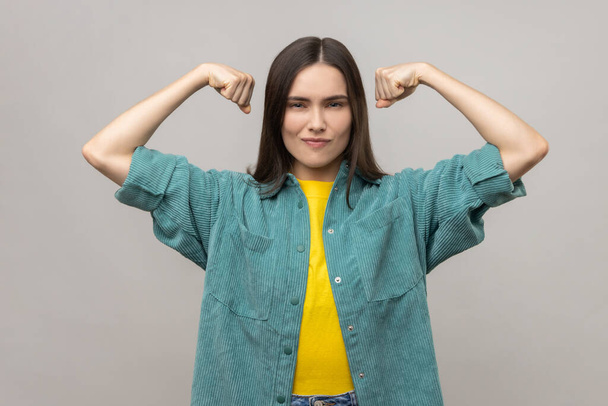 I am strong and independent. Confident proud woman showing biceps, expressing power ambitions to become successful, feminism concept, female rights. Indoor studio shot isolated on gray background. - Φωτογραφία, εικόνα