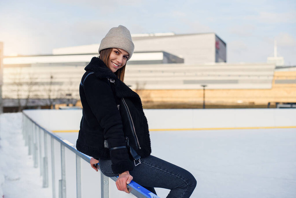 Happy beautiful woman at stylish jacket having fun, laugh on outdoor ice skating rink. Cheerful pretty young woman skate on Christmas ice rink. Winter holiday outside activity - 写真・画像