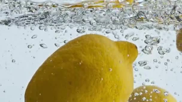 Limões tropicais a salpicar água de perto. Frutas azedas amarelas saltando líquido transparente. Citrinos saborosos para coquetel refrescante de verão. Tiro comercial de comida. Conceito vegetariano de alimentação saudável. - Filmagem, Vídeo
