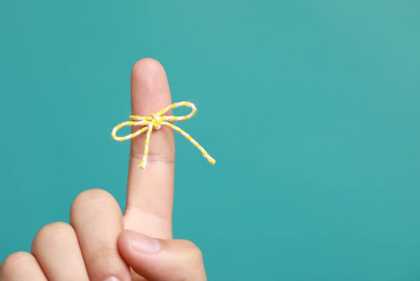 Man showing index finger with tied bow as reminder on turquoise background, closeup. Space for text - Photo, image