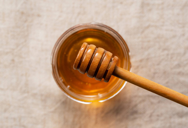 Honig im Glasgefäß und hölzerner Honigwagen auf Stoffhintergrund. Honig tropft aus dem Honigwagen. Blick von oben. - Foto, Bild