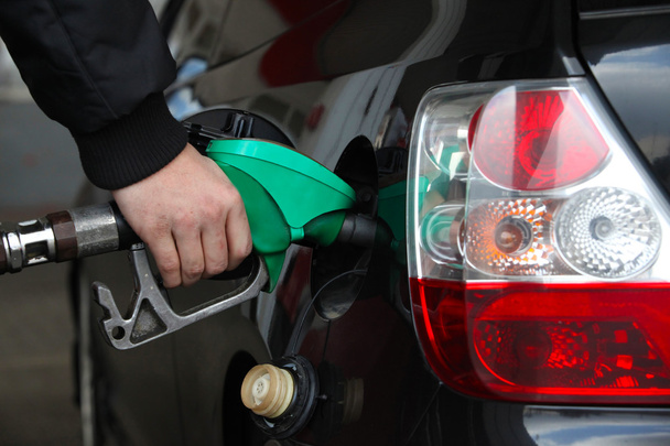 Мужская рука заправляет черный автомобиль топливом на заправочной станции
 - Фото, изображение