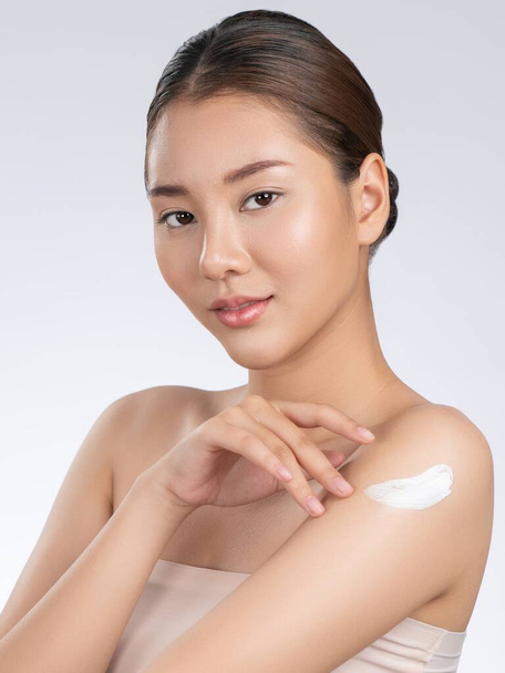Gorgeous girl with soft makeup applying moisturizing skincare cream on shoulder isolated over white background. Skincare cream applied by female model concept. - Photo, image