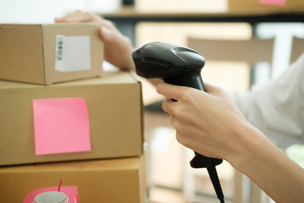 Female small online business owner holding scanner scanning parcel barcode tag before shipment at workplace. Woman selling products online, scanning parcel barcode. Online business concept. - Фото, зображення