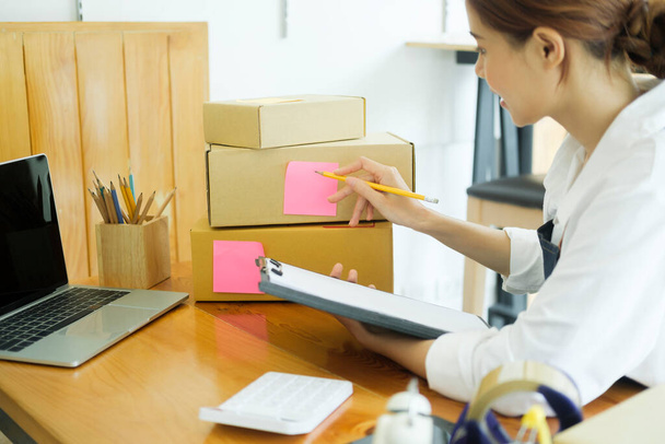 Asian female small online business owner packing boxes on table and checking retail order preparing for shipment. Online business, e-commerce concept. - 写真・画像