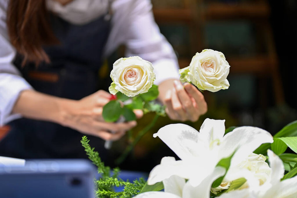 Professionelle Floristin oder Mitarbeiterin eines Blumengeschäfts arrangiert einen schönen Strauß und stellt einen weißen Rosenstrauß für ihre Kundin her. zugeschnittenes und Nahaufnahme-Bild - Foto, Bild