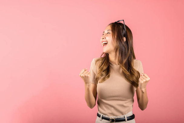 Happy Asian portrait beautiful cute young woman wear glasses makes raised hand up celebrating her winning success gesture, studio shot isolated pink background, Female excited say yes! with copy space - Foto, Imagem