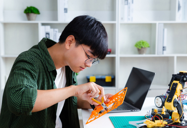 Asiatischer Teenager macht Roboterarm-Hausaufgaben-Projekt im Haus, Technologie der Robotik-Programmierung und MINT-Ausbildungskonzept. - Foto, Bild