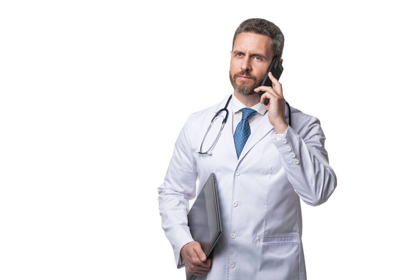 Serious doctor talking on mobile phone. Mobile physician holding laptop. Using mobile technology in healthcare. Ehealth. Telemedicine, copy space. - Photo, Image