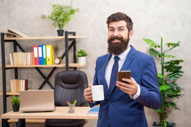 Happy man in suit smiling when got sms on smartphone in office, message. - Фото, изображение