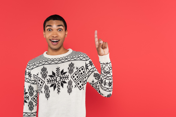 cheerful african american man in white sweater with winter pattern showing idea sign isolated on red - Fotoğraf, Görsel