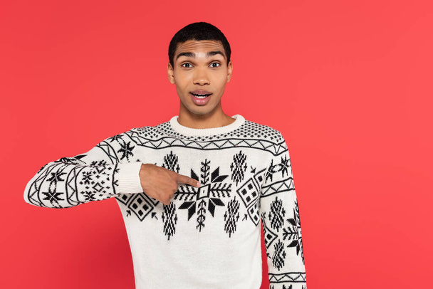 surprised african american man in sweater with winter pattern pointing with finger at himself isolated on red - Фото, зображення
