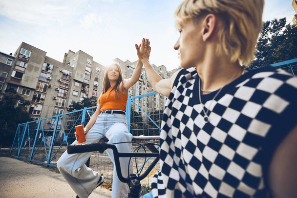 A teenage couple is giving high five to each other while sitting in an urban exterior. - Photo, Image