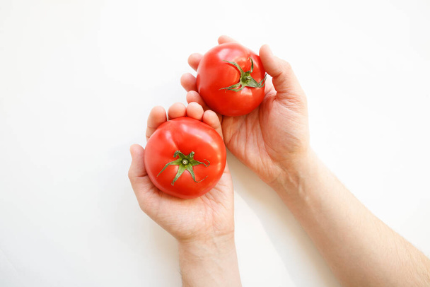 Man hands hold two red tomatoes on white background. Top view - Zdjęcie, obraz