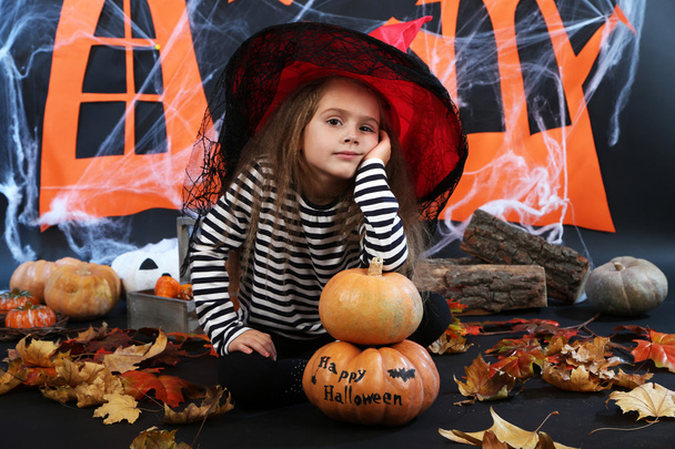 Маленька дівчинка Відьма в капелюсі з гарбузами на фоні прикрас на Хеллоуїн
 - Фото, зображення