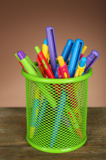 Colorful pens in green metal holder on wooden table and shaded color background - Fotó, kép