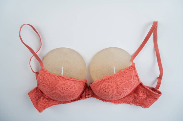 Breast implants in an orange bra on a white background - Fotoğraf, Görsel
