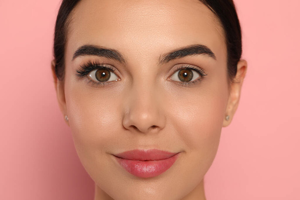 Beautiful young woman showing extended and ordinary eyelashes on pink background, closeup - Photo, Image