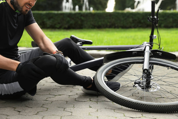Man with injured knee near bicycle outdoors, closeup - Фото, изображение