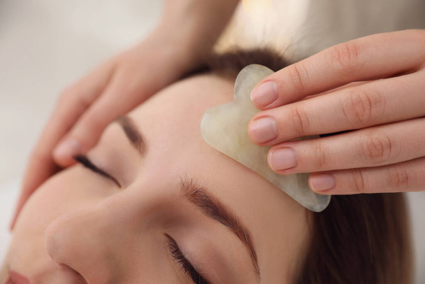 Young woman receiving facial massage with gua sha tool in beauty salon, closeup - Фото, зображення