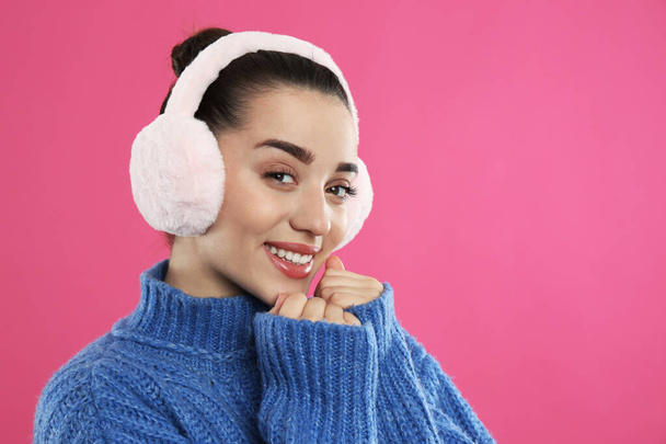 Beautiful young woman wearing earmuffs on pink background. Space for text - Foto, imagen