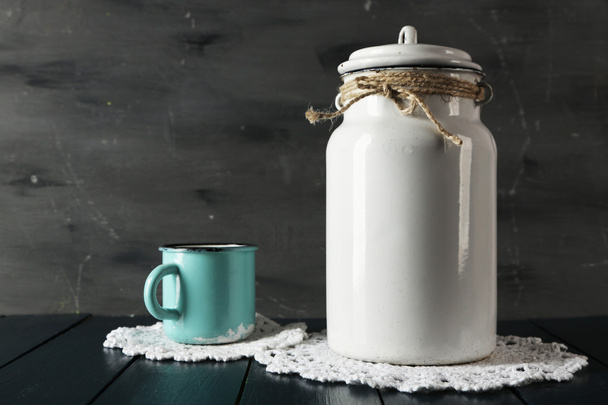 Milk can and cup on lace doily on wooden table and dark background - Φωτογραφία, εικόνα
