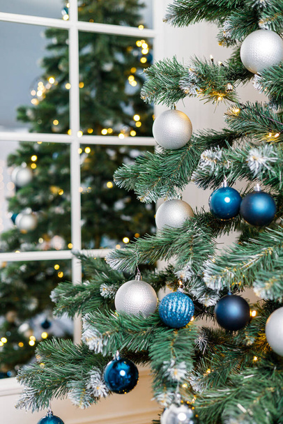 Vánoční stromek s modrými a stříbrnými hračkami. Slavnostně zdobený vánoční stromek s věnci. Symbol nového roku. - Fotografie, Obrázek