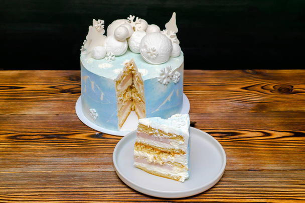 White blue sponge coconut delicious vanilla creamy frosting cake decorated with big round marshmallow, chocolate snowflakes, fir trees, mountain picture, cut piece sweet dessert with strawberry layer. - Fotó, kép