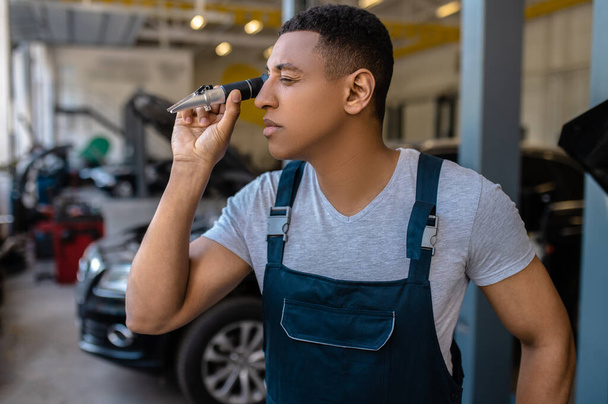 Waist-up portrait of a focused African American car mechanic looking inside the automotive spare part - Φωτογραφία, εικόνα
