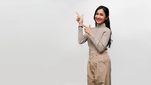Mulher asiática bonita jovem em roupas casuais sorrindo, apontando com duas mãos e dedos, em pé isolado sobre fundo cinza. espaço de cópia para publicidade ou apresentação de seu conteúdo. - Foto, Imagem