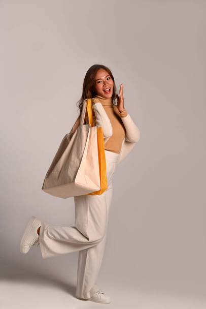 Full length excited woman carrying tote Eco bag standing over grey background. - Foto, immagini