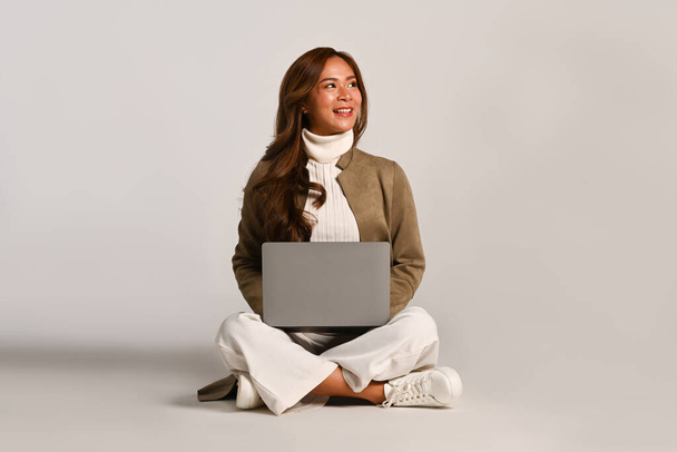 Belle femme dans des vêtements à la mode assis avec ordinateur portable sur studio blanc. Les gens et le concept technologique. - Photo, image