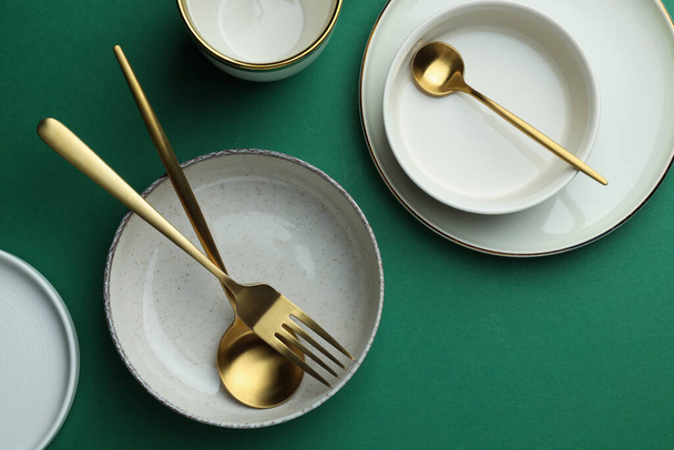 Stylish empty dishware and golden cutlery on green background, flat lay - Фото, зображення
