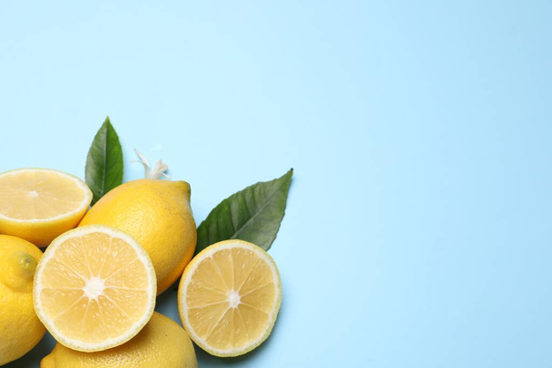 Many fresh ripe lemons with green leaves and flower on light blue background, flat lay. Space for text - Foto, imagen