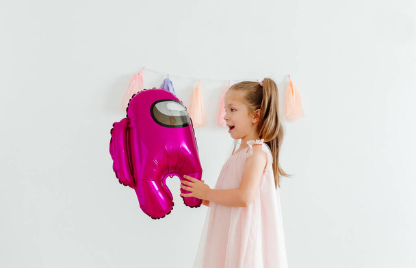 Cute zabawna dziewczynka z różowym wśród nas balon. Tassel girlanda na ścianie. Białe tło. - Zdjęcie, obraz