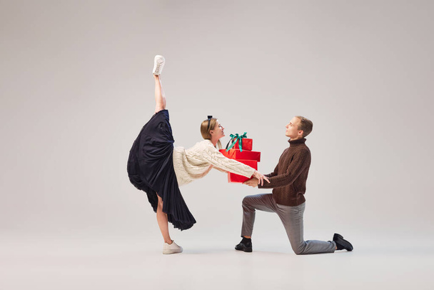 Portrait of beautiful man and woman, contemp ballet dancers in warm clothes in action, motion with bright festive gift boxes on gray background. Christmas, New year, holidays, 2023, party concept - Фото, зображення