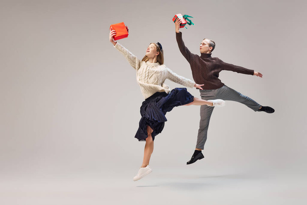 Dreams, love, happiness. Young and graceful couple of ballet dancers in warm winter clothes dancing with festive gift boxes on grey background. Christmas, New year, holidays, 2023, party concept - Фото, изображение