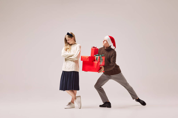 Love, tenderness and care. Flexible dancers, young happy couple in warm winter clothes dancing with festive gift boxes over grey background. Christmas, New year, holidays, 2023, party concept - Photo, image